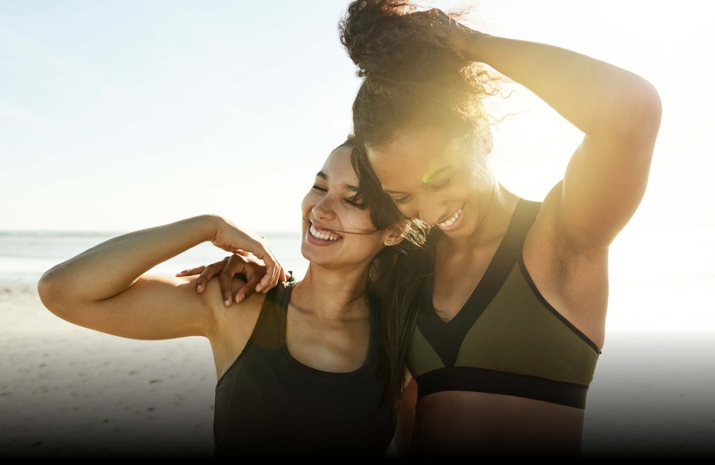 Due ragazze sorridono mentre si abbracciano al tramonto in spieggia